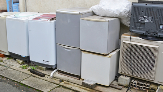 屋外に並べられた、回収対象となる洗濯機や冷蔵庫、エアコンの室外機、テレビなどの家電類