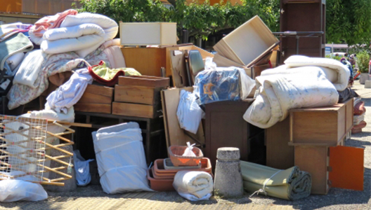 家具や寝具、収納用品などの不用品が屋外にまとめて置かれている回収前の様子。家庭から出た複数種類の不用品が一括で集められている。