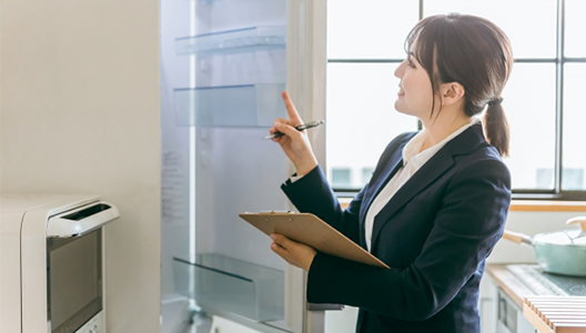 開いた冷蔵庫の中を確認しながら、チェックリストに記入するスーツ姿の査定スタッフ
