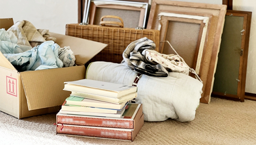 段ボール箱に入った衣類や積み上げられた本、カゴバッグなど、買取対象となる様々な生活雑貨