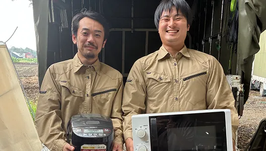 リサイクル可能な炊飯器と電子レンジを手に持ち、トラックの前で笑顔を見せるエコマックス埼玉のスタッフ